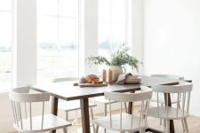 a small airy dining room with a stained table and vintage white chairs, some greenery is a very welcoming and cool space