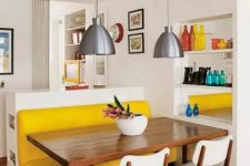 a small and bright dining space with a yellow upholstered bench, a stained table, white chairs, metal pendant lamps