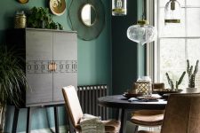 a small and chic dining space with an elegant dark-stained cabinet, green walls, a round table, leather chairs and a cluster of pendant lamps