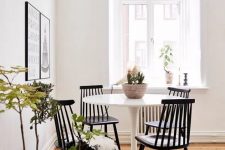 a small and cool Scandinavian dining nook with a white round chair, vintage black chairs, a black and white gallery wall and potted plants