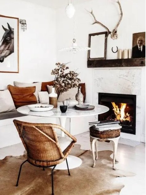 a small and cozy dining space with a fireplace, a round table, a built-in bench, a rattan chair and a leather stool