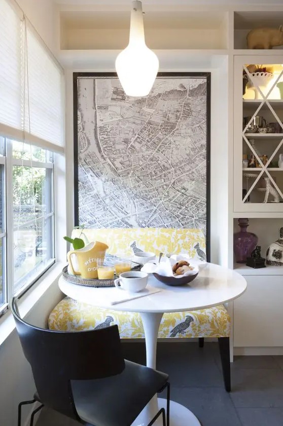 a small and cute dining nook with a colorful bench, a round table, a black chair, a pendant lamp and some yellow tableware