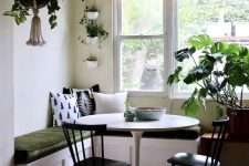 a small and lovely dining space with a corner bench, a round table and black chairs and lots of potted plants is a cool space for meals
