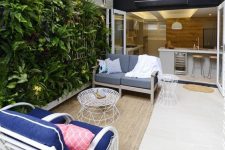a small and welcoming terrace with a white rattan chair, a living wall, a neutral and grey sofa, a white metal coffee table and spotlights