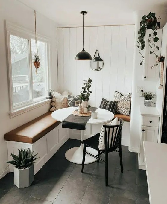 a small boho dining space with a built-in corner bench with a leather cushion, a round table, a black chair, a pendant lamp