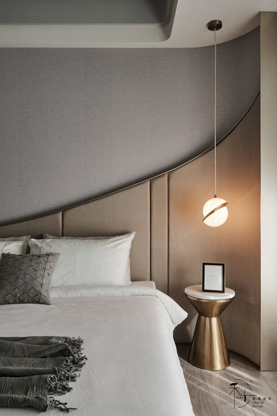 a small contemporary bedroom with much taste, with a paneled wall, a bed with neutral bedding, a pendant lamp and a gold nightstand