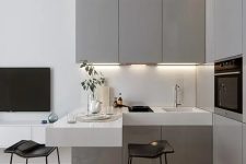 a small contemporary kitchen with sleek grey cabinets, a white floating countertop and a backsplash, some built-in appliances