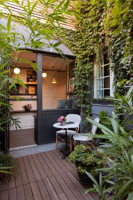 a small patio with a living greenery wall, potted greenery, a couple of rattan chairs and a small side table