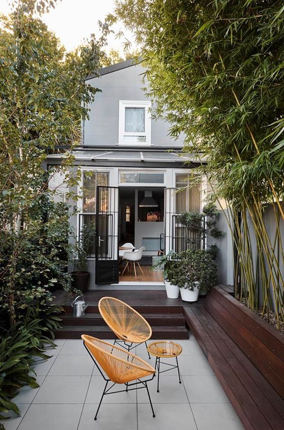 a small terrace with dark stained decks, a couple of round rattan chairs and a side table, lots of greenery around
