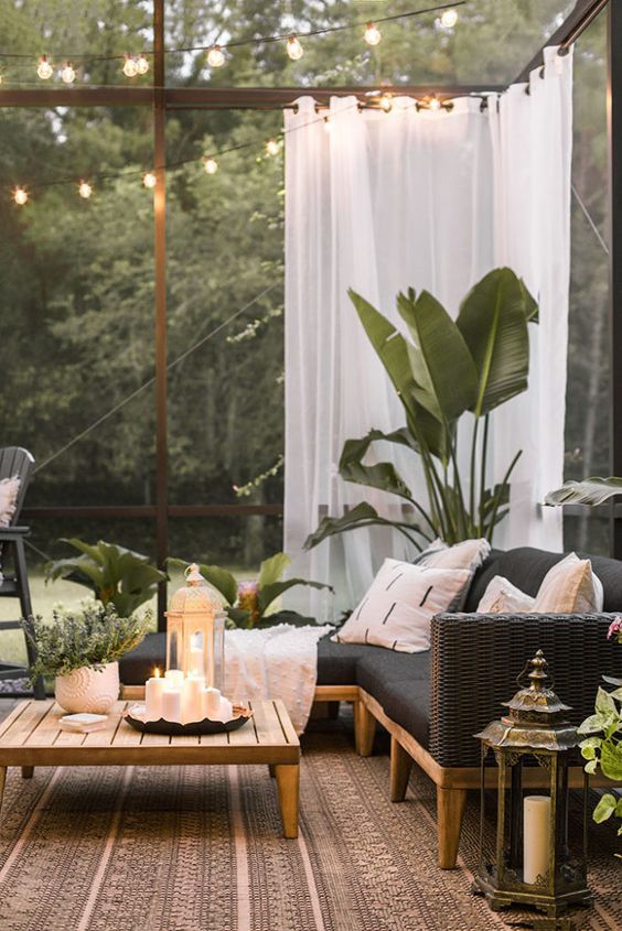 a small tropical terrace with a black wicker corner sofa, a low coffee table, lots of potted plants and candle lanterns