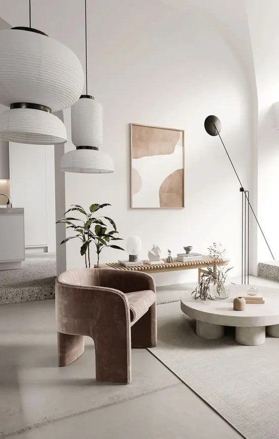 a sophisticated contemporary living room with a curved dusty pink chair, a round coffee table, a wooden bench, potted greenery, a statement artwork and lots of lamps