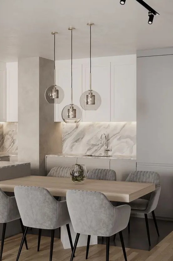 a sophisticated neutral dining space with a light-stained table, grey upholstered chairs, a trio of pendant lamps and built-in lights