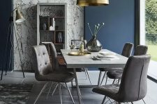 a stylish contemporary dining room with a glazed wall, a concrete table, grey upholstered chairs, a gold pendant lamp and candles