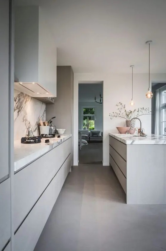 a stylish grey contemporary kitchen with sleek cabinets and a large kitchen island, a white stone backsplash and countertops and pendant lamps