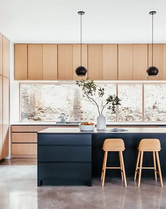 a stylish light stained kitchen with a large window backsplash, a navy kitchen island, black pendant lamps and tall stained stools is perfection