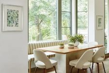 a stylish mid-century modern dining space by the window, with a large striped sofa, a table and creamy chairs and a gorgeous view