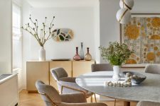 a stylish neutral dining room with a stone table, grey chairs, lovely sphere pendant lamps,a  gold credenza and a large artwork