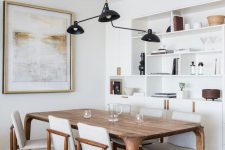 a stylish neutral dining space with a built-in storage unit, a stained table and creamy chairs, a black pendant lamp and an artwork
