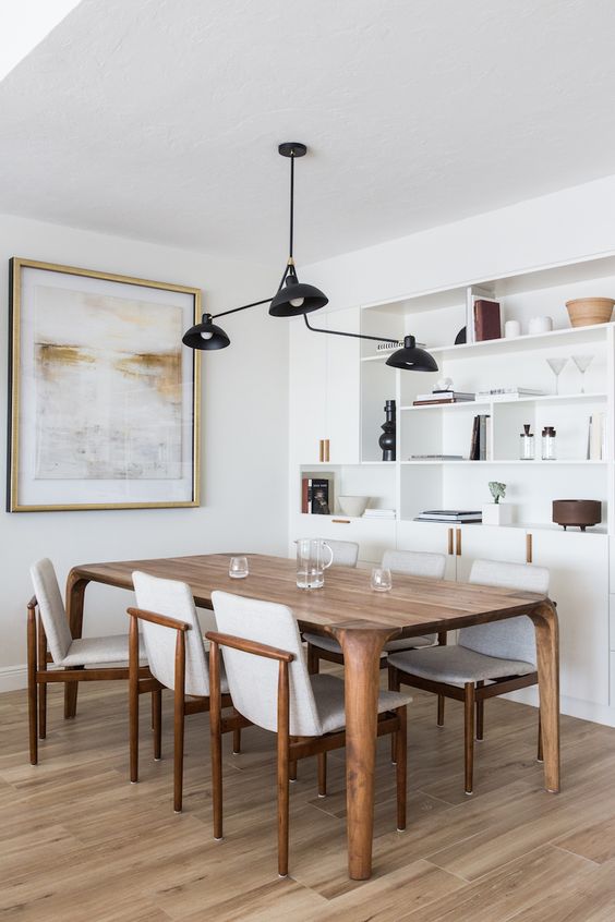 a stylish neutral dining space with a built-in storage unit, a stained table and creamy chairs, a black pendant lamp and an artwork