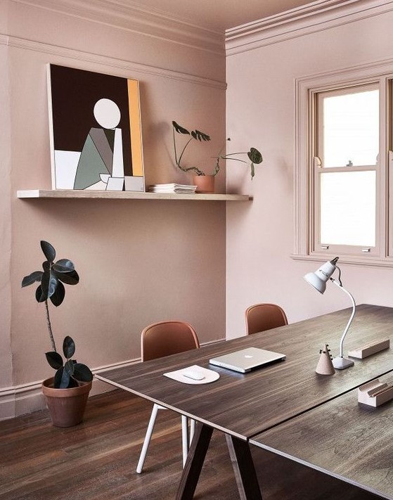 a stylish shared home office in pale pink, with two trestle desks, open shelving, potted plants and an abstract artwork