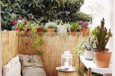 a tiny boho terrace with an upholstered bench, a wicker ottoman, a large plant stand and lots of potted plants around
