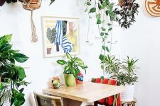 a tiny bright boho dining space with a wall-mounted table and stained chairs, potted greenery and bright art is all cool