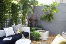 a tiny modern terrace with a wooden deck, a wall with greenery, a built-in sofa, a chair and a fountain plus a small table