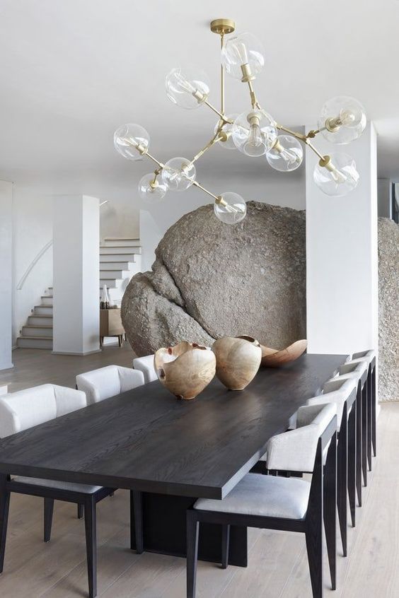 a unique contemporary dining room with a black table, white chairs, a huge rock and a cool chandelier with bubbles