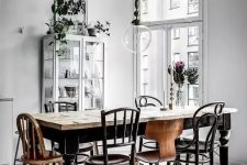 a vintage Nordic dining room with a vintage black dining table, mismatching chairs, a white glass cupboard and lots of potted plants