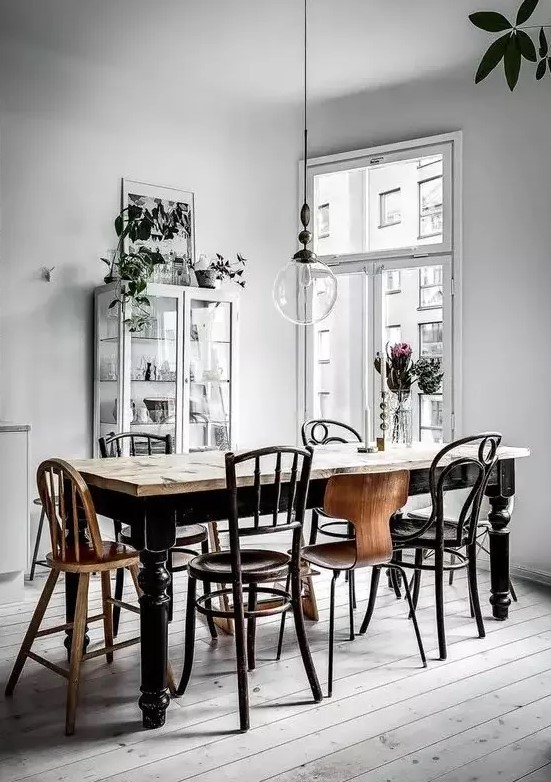 a vintage Nordic dining room with a vintage black dining table, mismatching chairs, a white glass cupboard and lots of potted plants