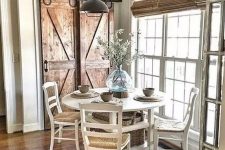 a vintage farmhouse dining nook with wooden doors, a white dining set, wicker shades and a metal lamp