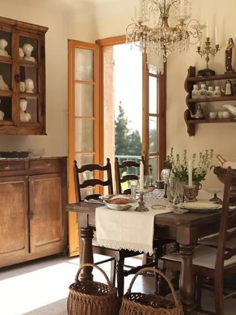 a vintage farmhouse dining room with stained furniture - a dining set, a wall-mounted shelf and some cabinets, a crystal chandelier
