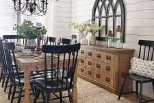 a vintage farmhouse dining space with black chairs, a light stained buffet and table, a metal chandelier
