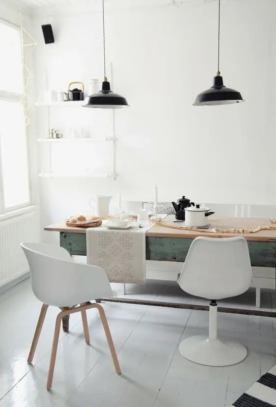 a vintage-inspired Nordic dining room with a long blue table, mismatching white chairs, a lightweight wall shelf and black pendant lamps
