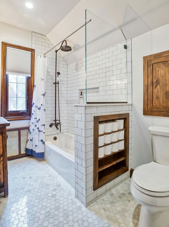 a vintage inspired bathroom with white and marble tiles, with a half wall that has soem integrated storage space, touches of stained wood for more coziness