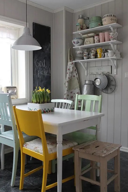 a vintage neutral dining space with shelves on the wall, a white table and mismatching chairs, pastel floral prints and a chalkboard to leave notes
