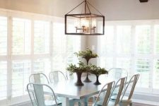 a vintage rustic dining space with a white dining table, white metal chairs, greenery and a metal frame pendant lamp