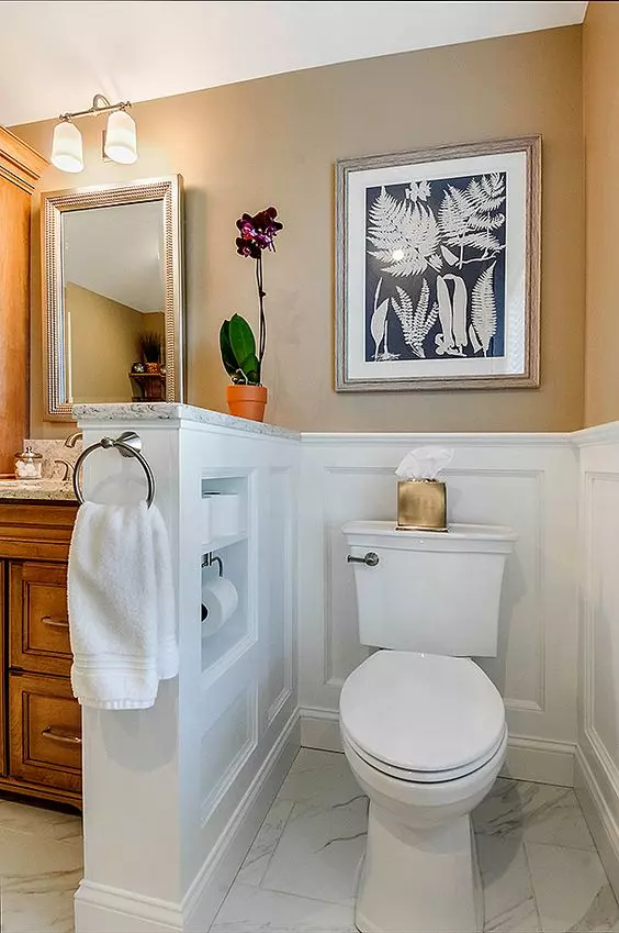 a vintage tan-colored bathroom with white paneling, a half wall that hides the toilet and can be used for storing things