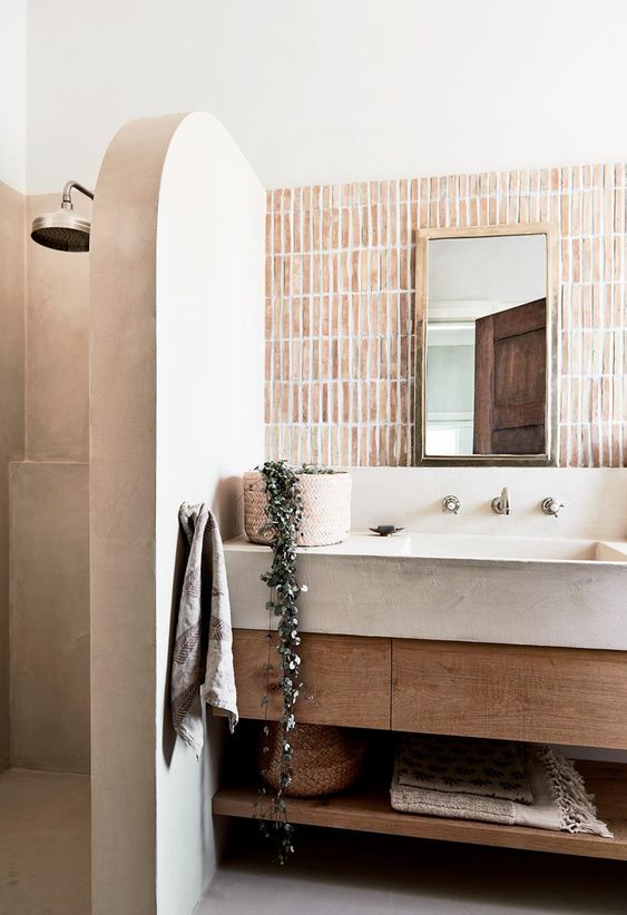 a warm-colored bathroom with skinny tiles, a tadelakt half wall that separates the shower space from the rest of the bathroom