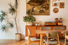 a warm-colored mid-century modern dining room with a stained table and grey chairs, a stylish credenza, a cluster of pendant lamps and greenery