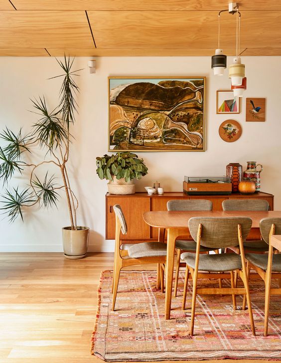 a warm-colored mid-century modern dining room with a stained table and grey chairs, a stylish credenza, a cluster of pendant lamps and greenery