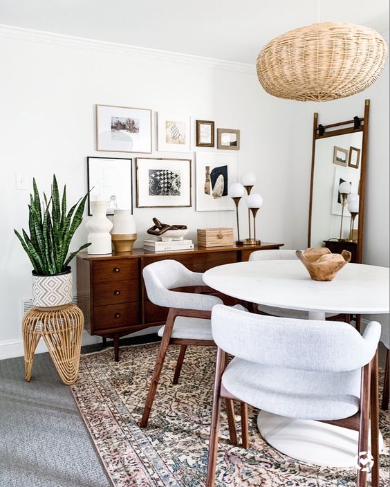 a welcoming mid century modern dining room with a stained credenza, a white table and neutral chairs, a woven pendant lamp, a gallery wall