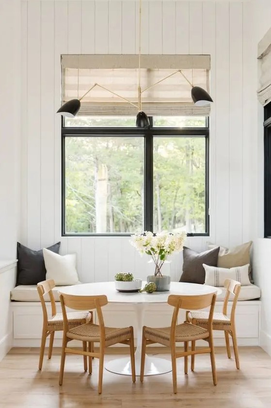 a welcoming modern farmhouse dining space with a built-in bench, a round table, woven chairs, touches of black and woven shades