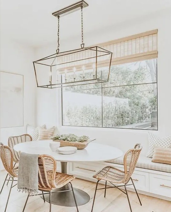 a welcoming modern farmhouse neutral dining space with a built-in bench, an oval table, rattan chairs, a chic brass pendant lamp
