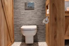 a welcoming neutral bathroom with pebbles on the floor, a stained wood wall, a stained wood half wall as a space divider and a storage unit