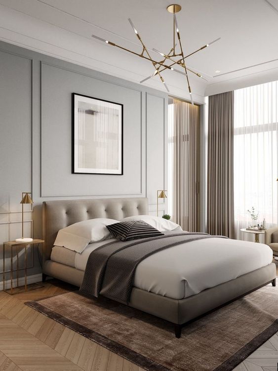 a welcoming neutral bedroom with grey walls, a taupe upholstered bed and lightweight nightstands, a catchy chandelier