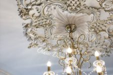 a white and gold ceiling medalltion with floral motifs and a chic crystal chandelier with candles and crystals is wow