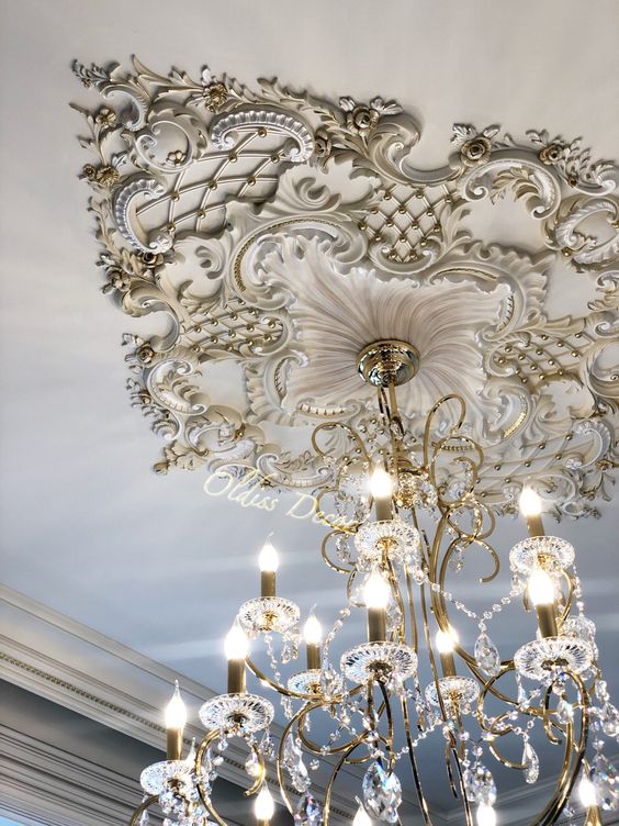 a white and gold ceiling medalltion with floral motifs and a chic crystal chandelier with candles and crystals is wow