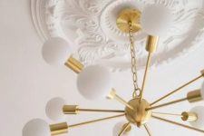 a white ceiling medallion with a gold sunburst chandelier – the vintage look of the medallion and modern look of the chandelier contrast