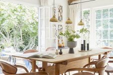 an airy neutral dining room with a stained table and chairs, greenery, a gold chandelier and a lovely garden view
